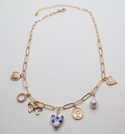 Charm Necklace. This gold-tone necklace features a combination of unique, eye-catching charms, including a delicate pearl, a floral-inspired heart, and intricate coin pendants.