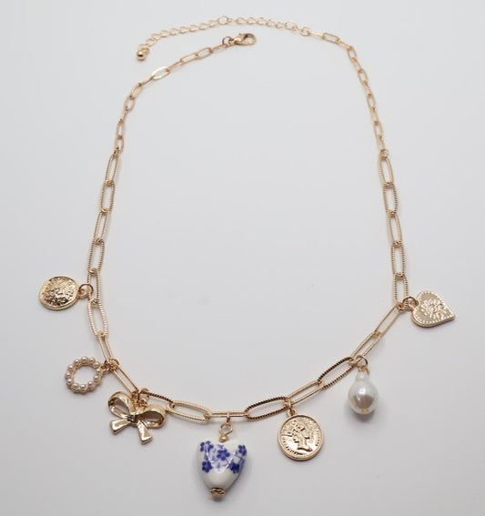 Charm Necklace. This gold-tone necklace features a combination of unique, eye-catching charms, including a delicate pearl, a floral-inspired heart, and intricate coin pendants.