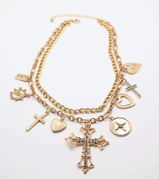 Charm Necklace. This beautifully layered gold-tone necklace features an enchanting collection of delicate charms, including graceful hearts, intricate crosses, and classic coin pendants. The centerpiece, a stunningly detailed cross.
