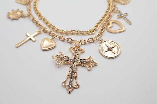 Charm Necklace. This beautifully layered gold-tone necklace features an enchanting collection of delicate charms, including graceful hearts, intricate crosses, and classic coin pendants. The centerpiece, a stunningly detailed cross.