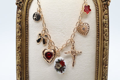  Vintage Charm Necklace. Featuring a gold-tone chain adorned with an exquisite collection of charms, including a rose-adorned heart, a dainty bow, a floral oval pendant, and a radiant cross.