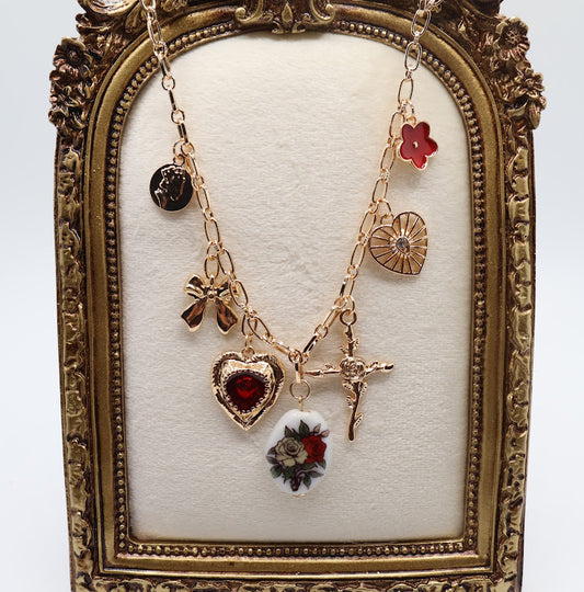  Vintage Charm Necklace. Featuring a gold-tone chain adorned with an exquisite collection of charms, including a rose-adorned heart, a dainty bow, a floral oval pendant, and a radiant cross.