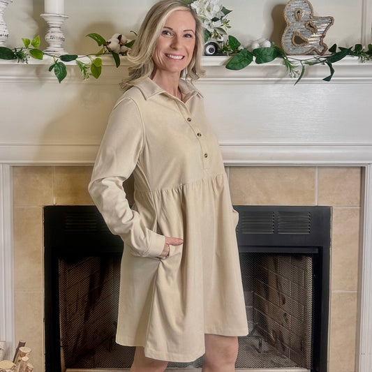 Woman in a beige dress standing in front of a fireplace