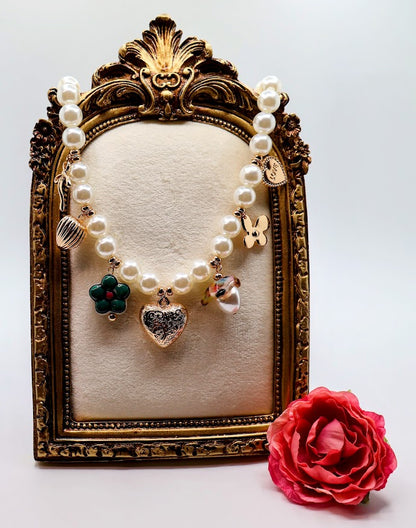 Pearl Charm Necklace is a graceful blend of timeless elegance and whimsical charm. Featuring a strand of lustrous pearls adorned with delicate gold-tone charms, including hearts, flowers, and a touch of sparkle.