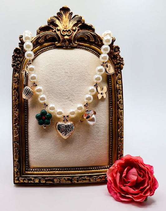 Pearl Charm Necklace is a graceful blend of timeless elegance and whimsical charm. Featuring a strand of lustrous pearls adorned with delicate gold-tone charms, including hearts, flowers, and a touch of sparkle.