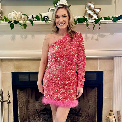 Woman in a pink sequined dress with feather details standing in front of a decorated fireplace.