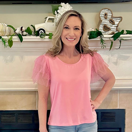 Woman wearing a pink blouse with sheer sleeves standing in front of a decorated fireplace.