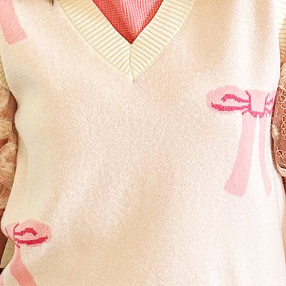 A woman wearing a cream knit sweater vest with pink bow details, sheer lace puff sleeves, and a pink skirt, standing in front of a fireplace.