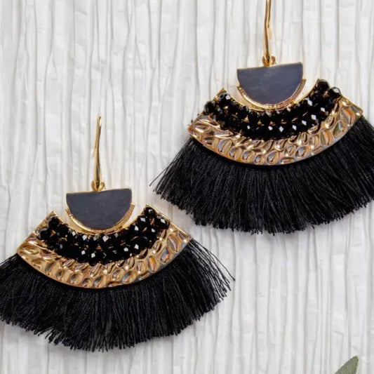 Black tassel earrings with gold accents on a wooden surface