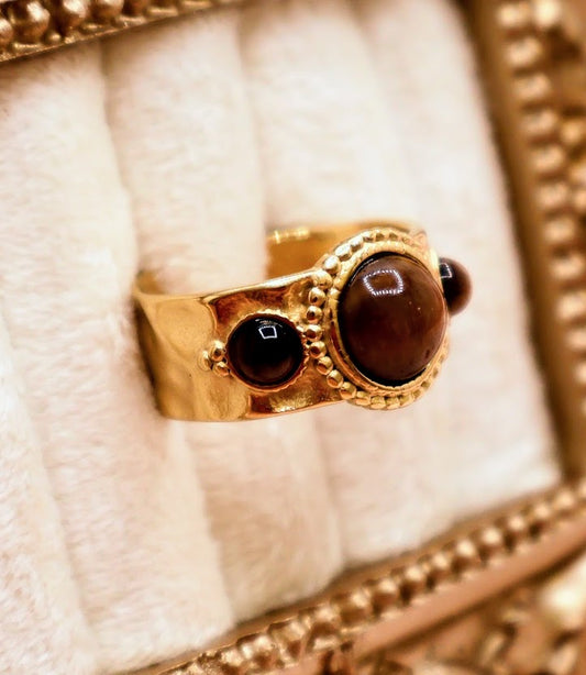 Ring is a captivating blend of warmth and mystique, making it a standout addition to any jewelry collection. Featuring a luminous round amber-toned centerpiece flanked by two smaller dark accent stones.