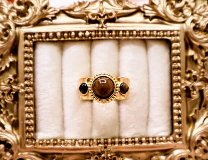 Ring is a captivating blend of warmth and mystique, making it a standout addition to any jewelry collection. Featuring a luminous round amber-toned centerpiece flanked by two smaller dark accent stones.