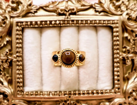 Ring is a captivating blend of warmth and mystique, making it a standout addition to any jewelry collection. Featuring a luminous round amber-toned centerpiece flanked by two smaller dark accent stones.