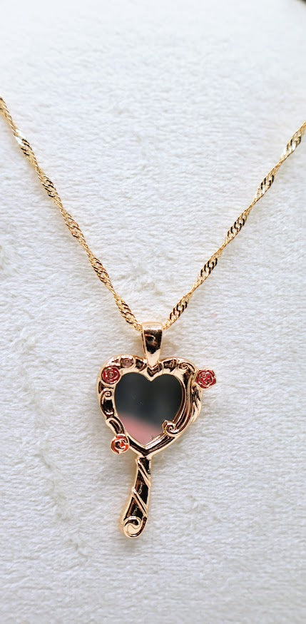 ose Mirror Necklace is a stunning symbol of elegance and charm. The heart-shaped pendant, designed as a petite mirror, features intricate gold swirls and delicate pink rose accents that add a romantic touch.