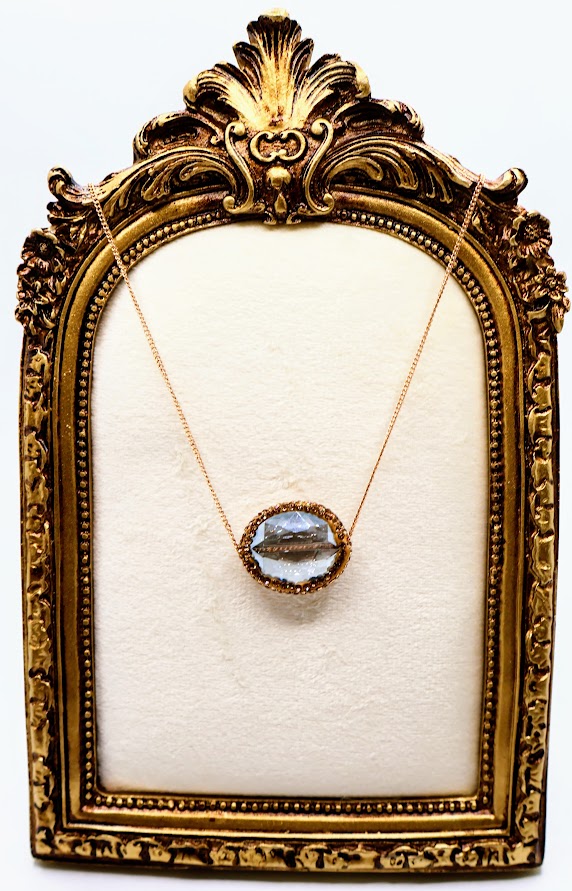 Necklace with a gleaming oval crystal framed in a warm golden setting, suspended from a fine gold chain.