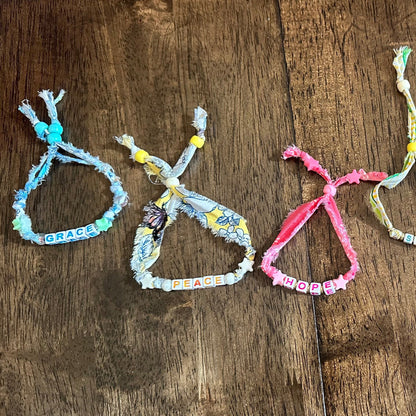 Four colorful woven rope bracelets with beads, arranged vertically on a dark brown wooden surface.