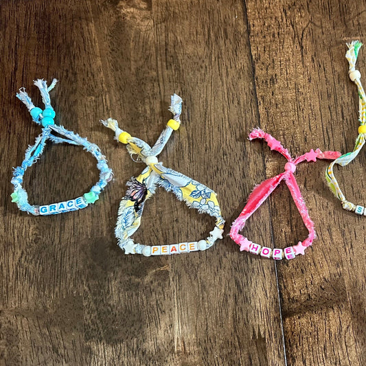 Four colorful woven rope bracelets with beads, arranged vertically on a dark brown wooden surface.