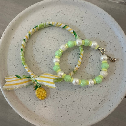 A set of two beaded and ribbon bracelets in pastel green, white, and yellow, displayed on a speckled ceramic plate.
