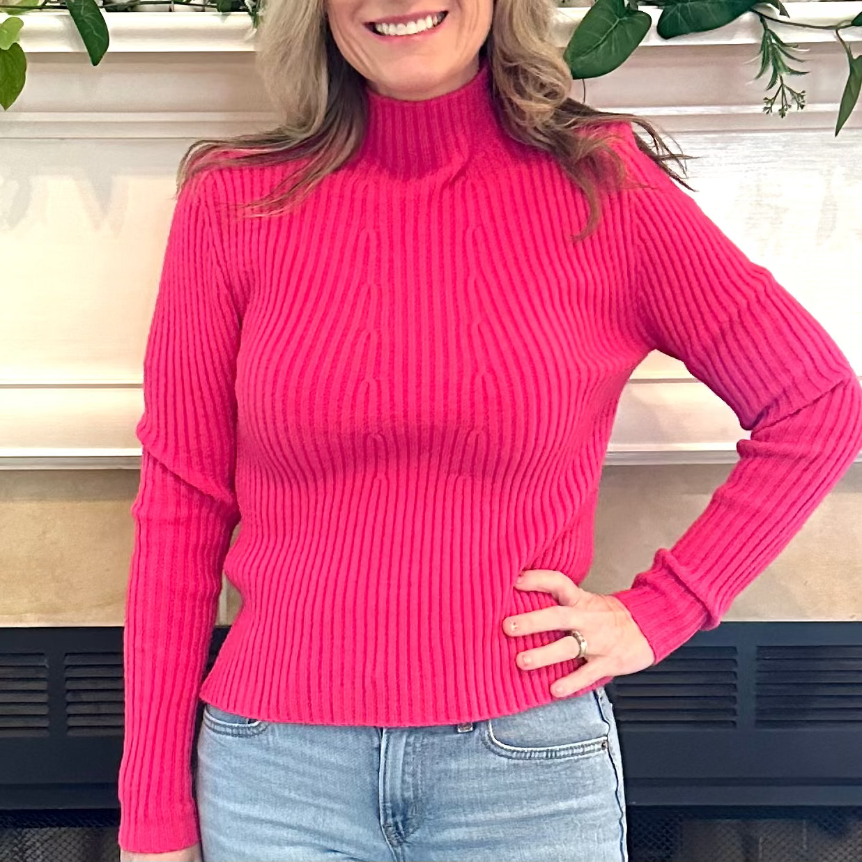 Person wearing a bright pink ribbed sweater and blue jeans indoors.