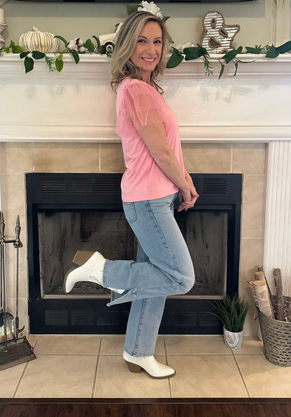 Woman in pink shirt and jeans standing in front of a fireplace with decorative items on the mantel.