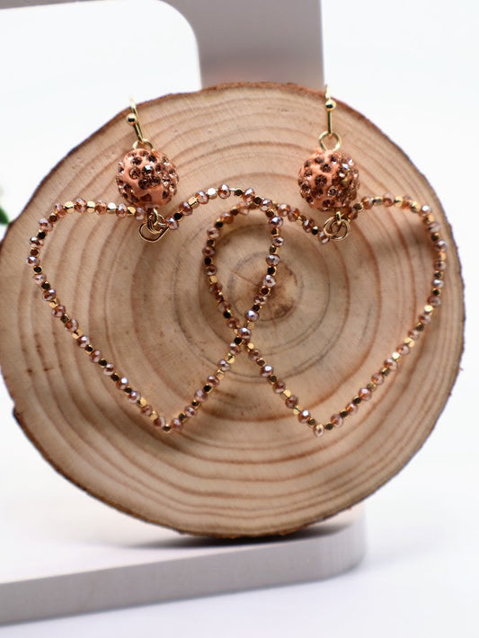 Rose gold heart-shaped earrings on a wooden block