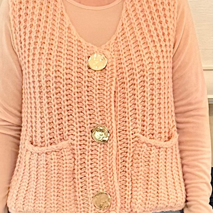 Person wearing a pink knitted vest with buttons
