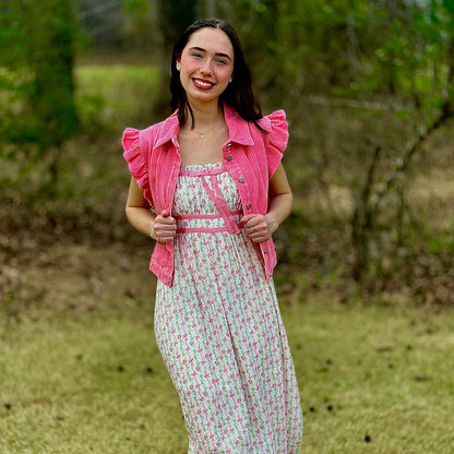 A woman stands outdoors on grass wearing a white midi dress with a pink floral print, a matching pink ruffled jacket, and white flats.