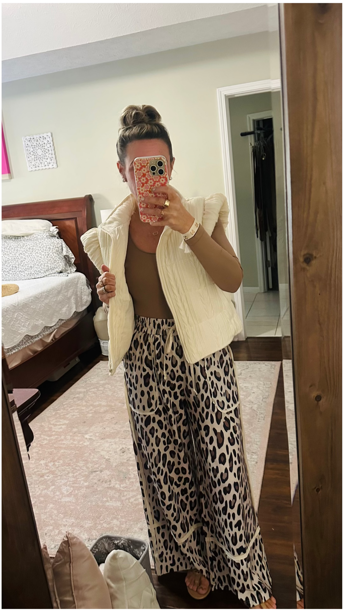Person wearing a beige vest and leopard print pants in a bedroom.