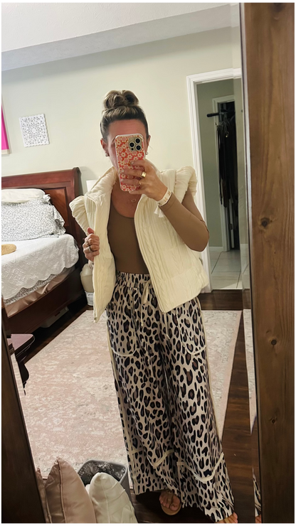 Person wearing a beige vest and leopard print pants in a bedroom.