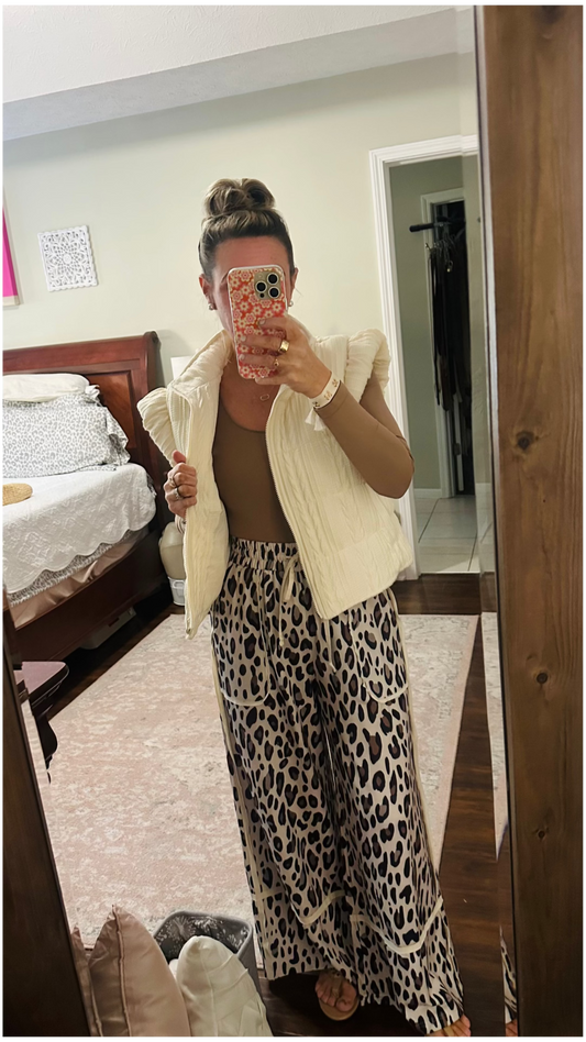 Person wearing a beige vest and leopard print pants in a bedroom.