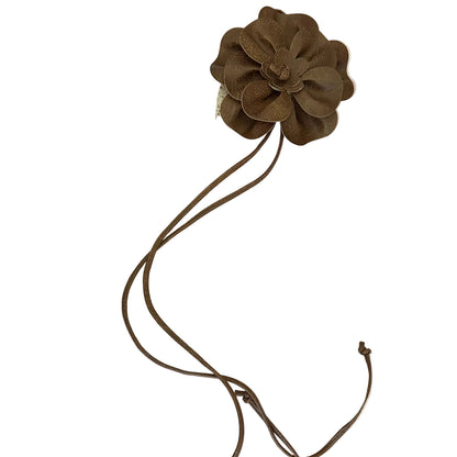 A brown faux-leather flower waist accessory with a long adjustable cord, laid flat on a pink and white marble-patterned surface.