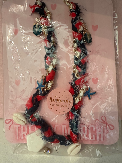 Necklace with starfish and shell charms in clear packaging on a pink background