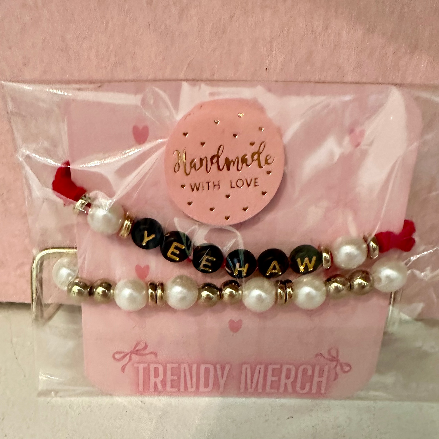 Set of beaded bracelets with a 'Handmade with Love' tag on a pink card, against a light pink background.