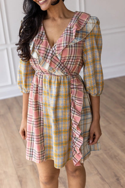 Plaid Ruffle Wrap Dress. Featuring a mix of soft plaid patterns, a flattering wrap design, and ruffled details along the neckline and hem.