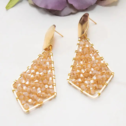 Gold and beige beaded earrings on a white background with purple flowers.