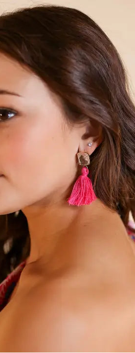 Woman wearing pink tassel earrings with a neutral background