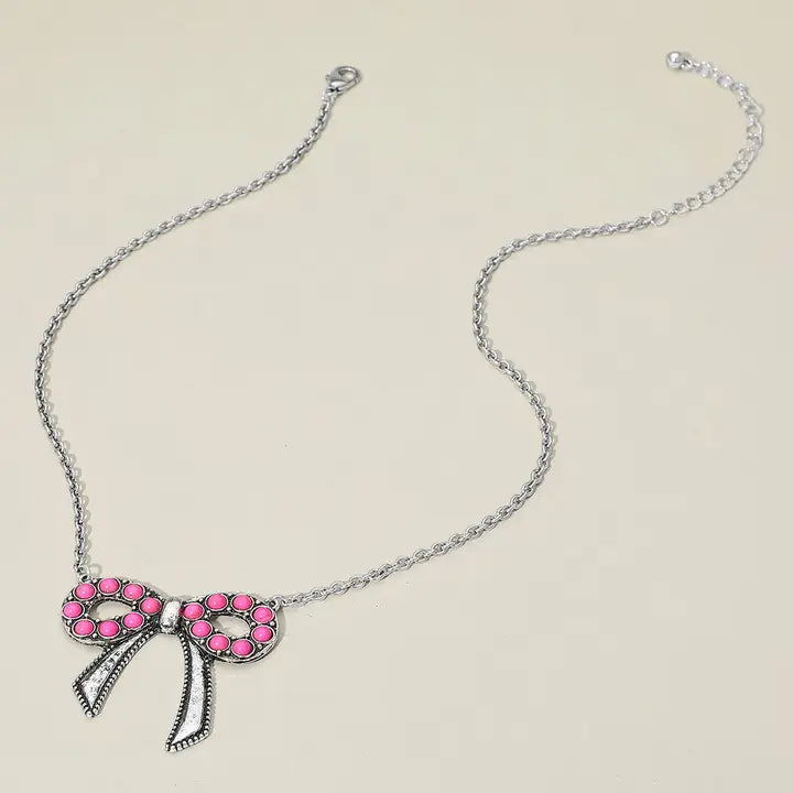 Necklace with a pink bow pendant on a beige background