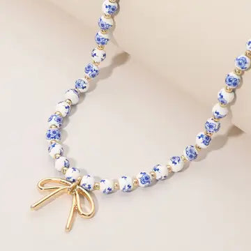 Necklace with floral beads and a gold bow charm on a beige background