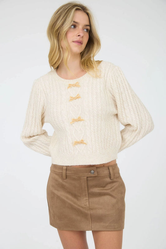 Cream Velvet Bow Cable Knit Sweater is a cozy and stylish addition to your wardrobe. Featuring a classic cable knit pattern and a round crew neckline.