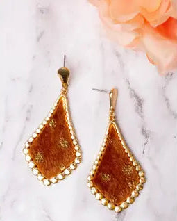 Gold teardrop earrings on a marble surface with a floral background