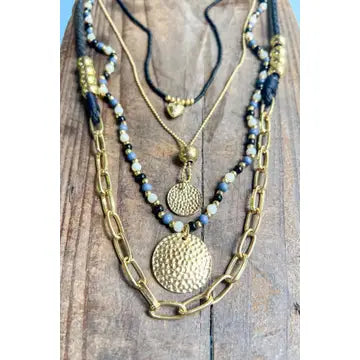 Three layered necklaces with gold chains and beaded sections on a wooden surface