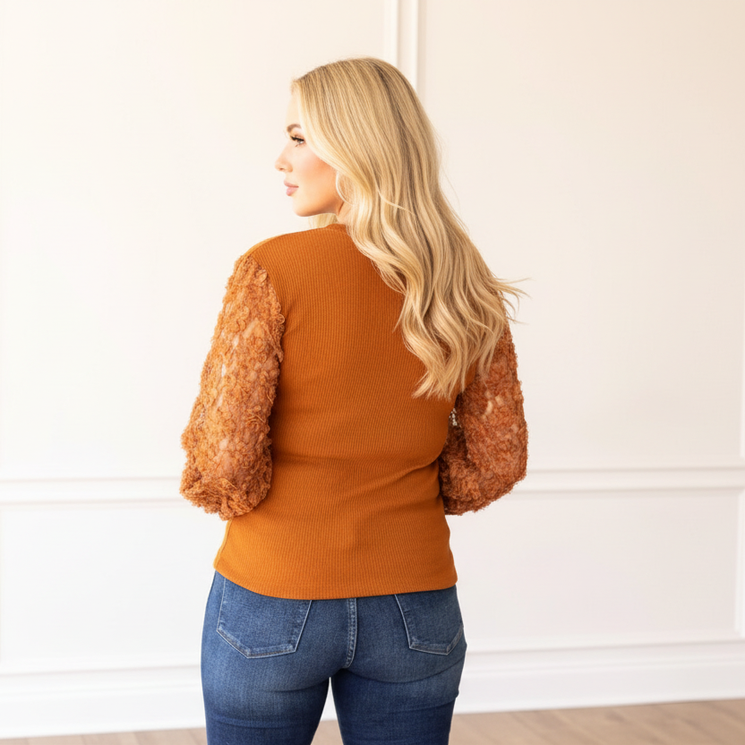 Woman wearing a rust-colored sweater with fur sleeves against a white paneled wall.