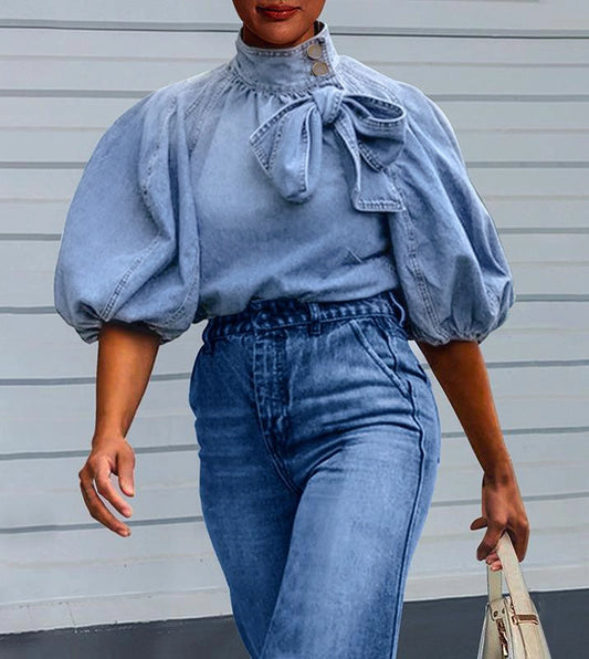  Puff Sleeve Denim Blouse is a stylish and versatile piece that combines casual comfort with a chic design. Featuring 3/4-length loose puff sleeves and a high neckline adorned with a statement bow.