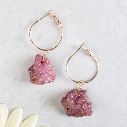 Gold hoop earrings with pink stone drops on a light background